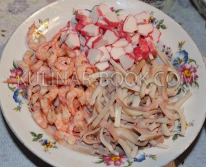 Очищенные креветки, крабовые палочки и кальмары нарезанные полосочками лежат в тарелки